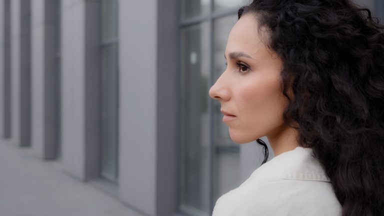 Close up back view Caucasian pensive thoughtful brunette lady with long curly hair looking away thinking dreaming pondering think waiting standing outdoors in city calm Latina Hispanic woman outside. High quality 4k footage